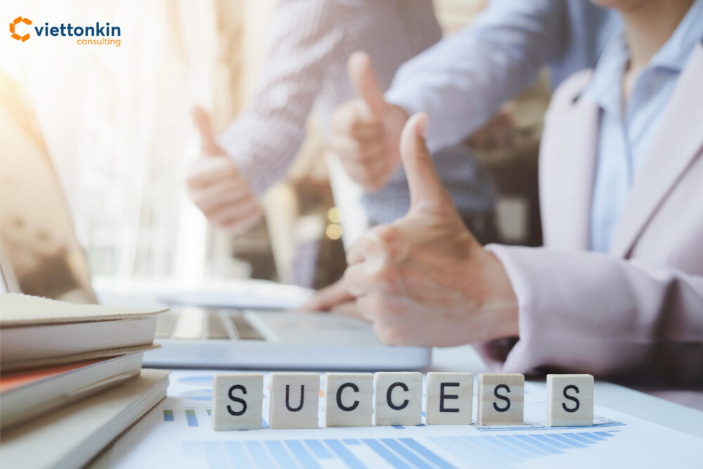 Business teamwork success concept with people giving thumbs up behind wooden blocks spelling SUCCESS on office desk